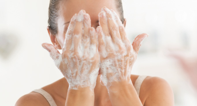 Frau reinigt ihr Gesicht mit einem sanften, cremigen Reinigungsschaum. Symbolisch für eine gründliche Hautreinigung.